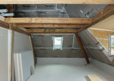 Dachgeschoss in der Sanierungsphase: Holzbalken, neu eingebrachte Dämmfolien und Gipskartonplatten signalisieren laufende Renovierungsarbeiten am Innenraum.